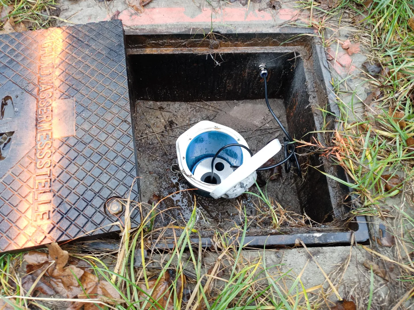 Geöffnete Grundwassermessstelle mit eingebautem Logger und Kabeldurchführung.