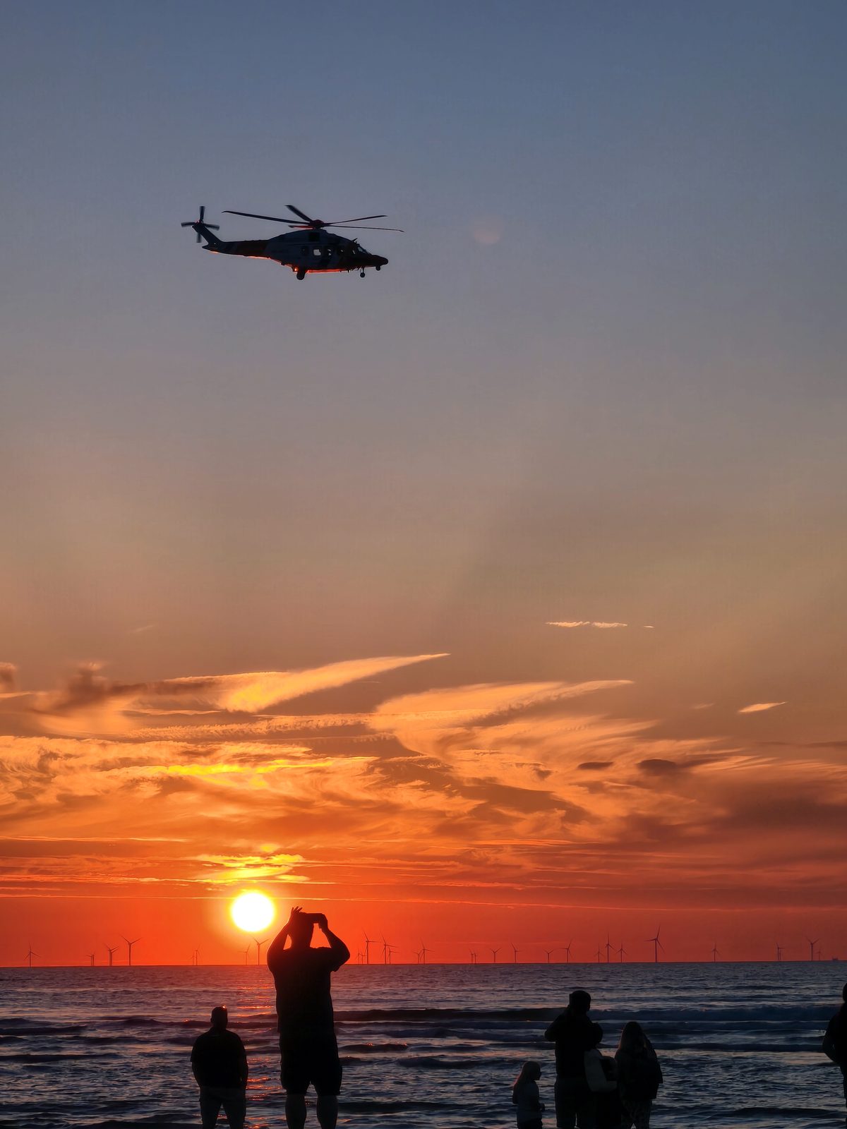 Rettungshubschrauber über Sonnenuntergang am Meer – Symbol für Frühwarnung und Einsatz bei Hochwasserlagen