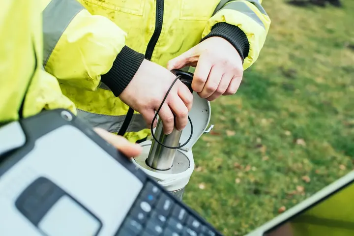 Techniker prüft einen Sensor an einer Messstelle, daneben ein Feldrechner