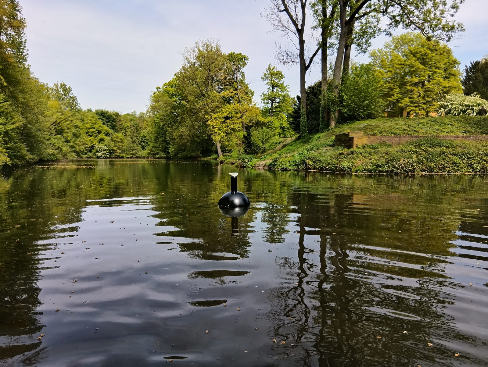 Schwarze Messboje schwimmt auf einem ruhigen Parkteich im Frühling