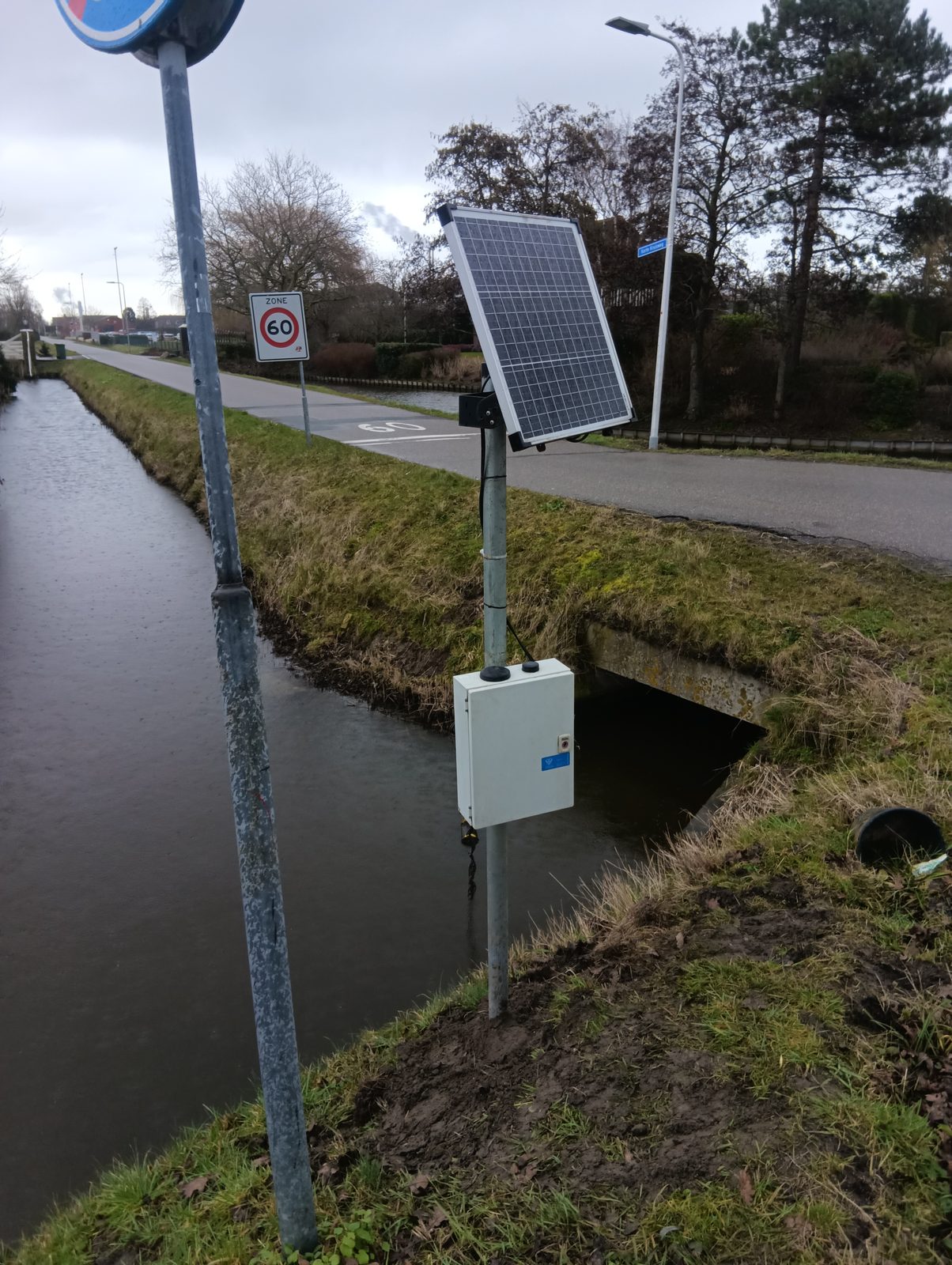 Pegelmessstelle an einem Straßendurchlass in den Niederlanden, Solarpanel und Sensorkasten