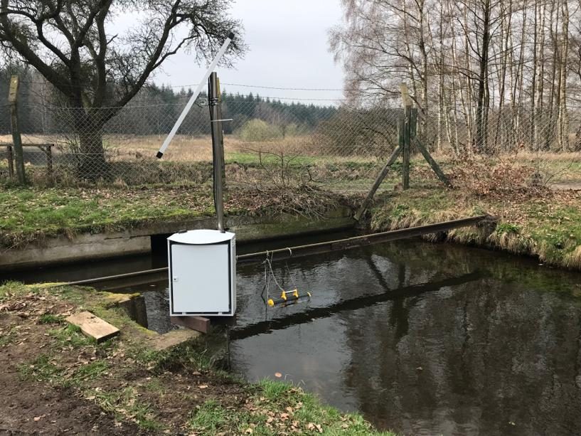 Pegelschrank am eingezäunten Wassergraben in der Heide, Messeinrichtung im Schutzgehäuse
