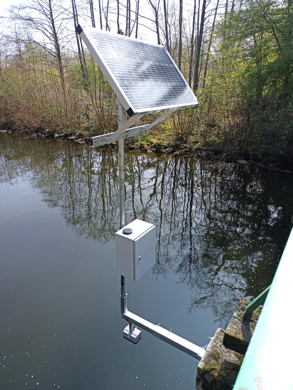 Hochgesetzter Solarpanel-Arm über einem Forstteich, Logger über der Wasserfläche