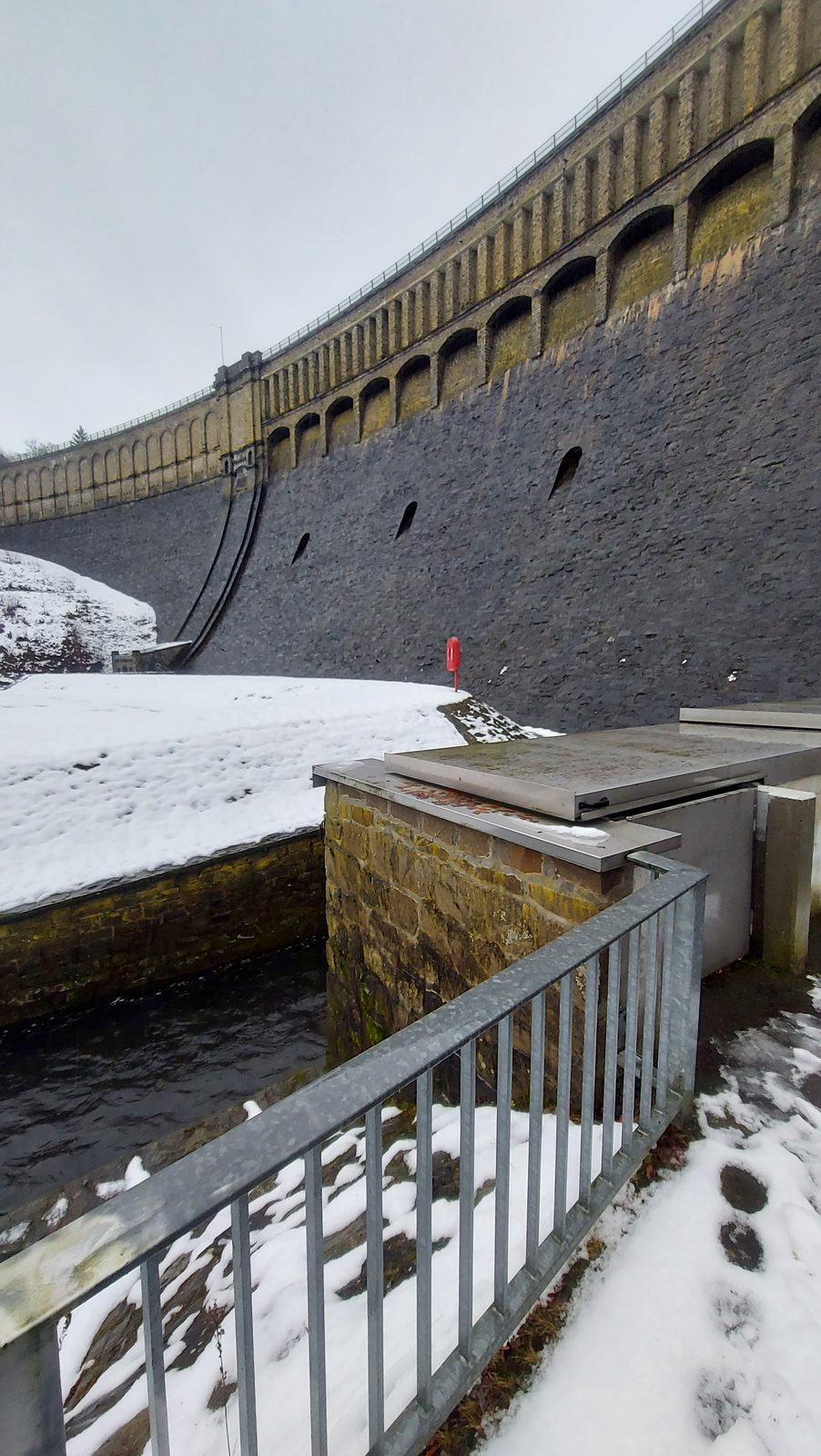Bruchstein-Staumauer mit Auslass im Winter, Pegelinstallation am Mauerfuß