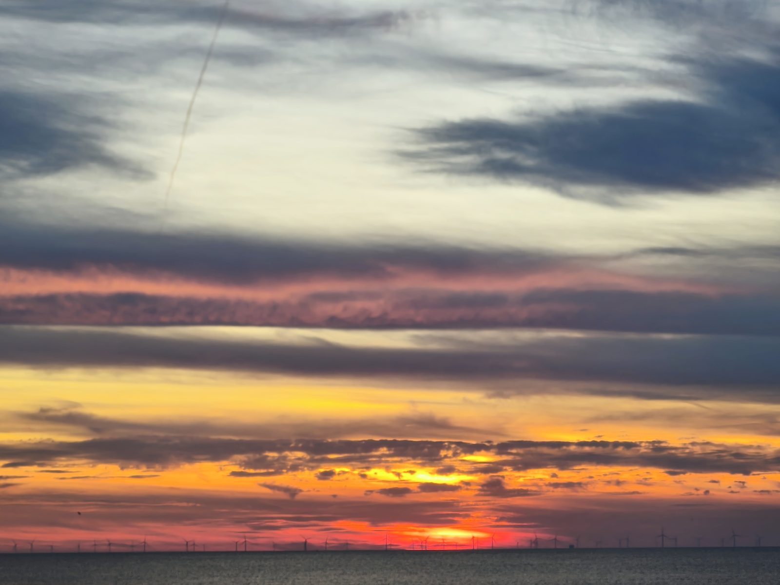 Sonnenuntergang über dem Meer mit Windkraftanlagen am Horizont – Klima- und Forschungsmonitoring